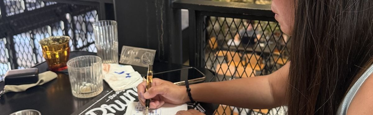 Quynh sketching warm-up icons in a notebook with a fountain pen at a cafe table