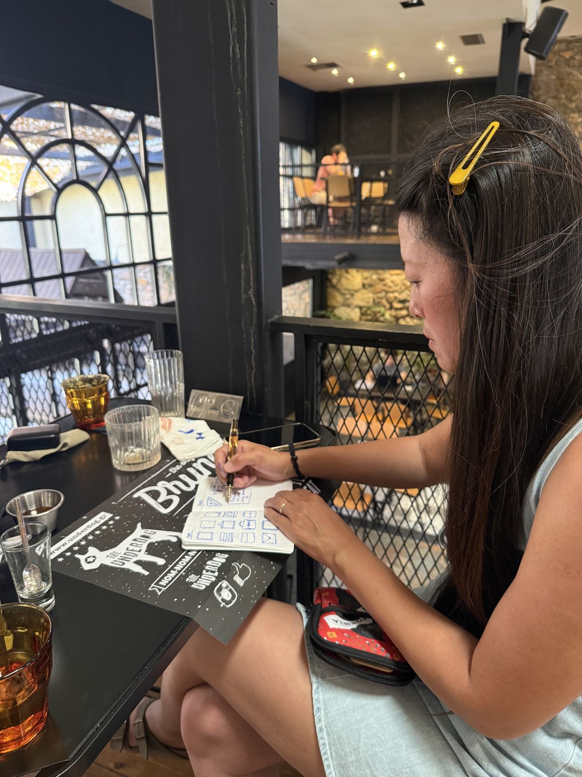 Quynh sketching warm-up icons in a notebook with a fountain pen at a cafe table